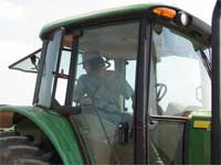 photo showing Dr. Joe Omielan in the cabin of the John Deere tractor monitoring the drill planter used for seeding the soybean test plots