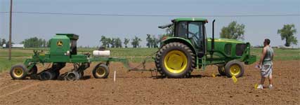 photo showing research intern assisting tractor operator with proper row alignment while using the drill planter