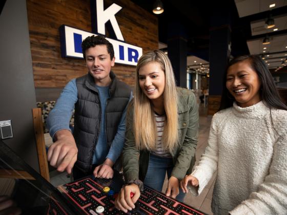 A group of students play pac-man on an arcade machine in K-Lair.