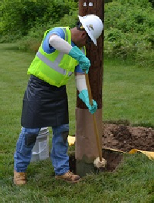 Applying preservative paste to base of utility pole