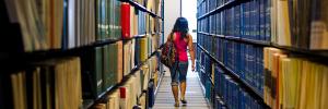 Student walking between rows of books in library