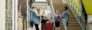 Image of students discussing a large piece of art hung in the Art and Visual Studies Building main lobby.