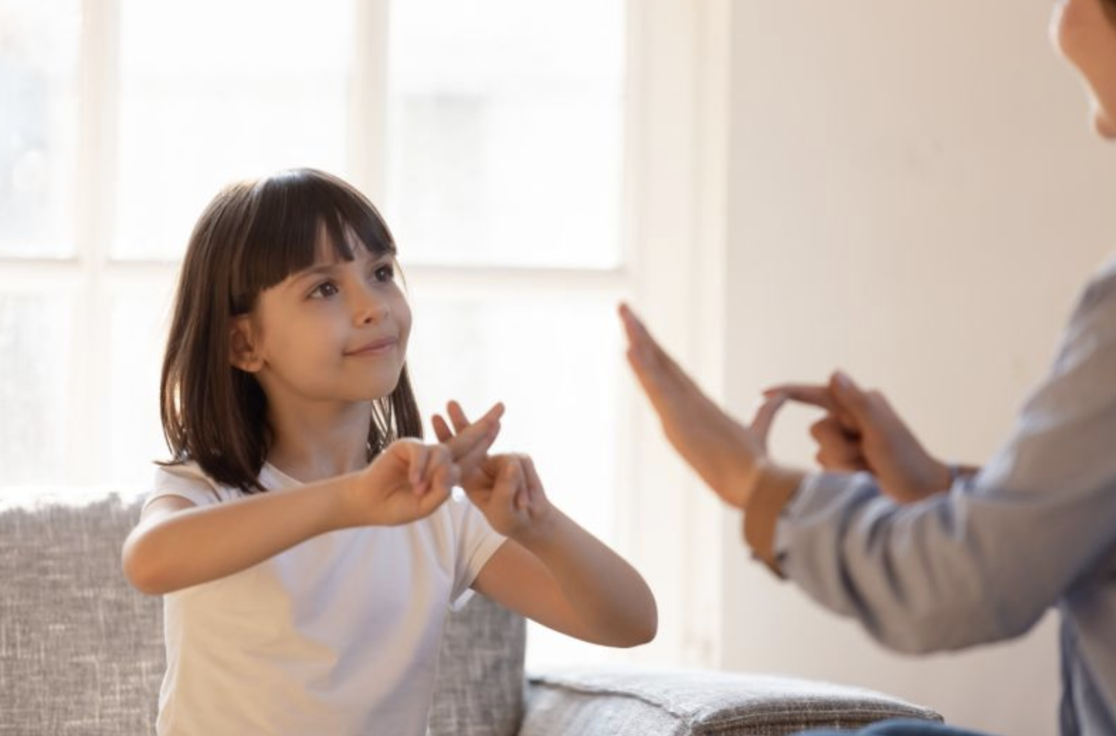 A black-haired Hispanic child talks in sign language to an adult