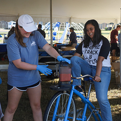 A University of Kentucky student smiling as she makes a smoothie by pedaling on a bicycle at the Sustainability Festival.