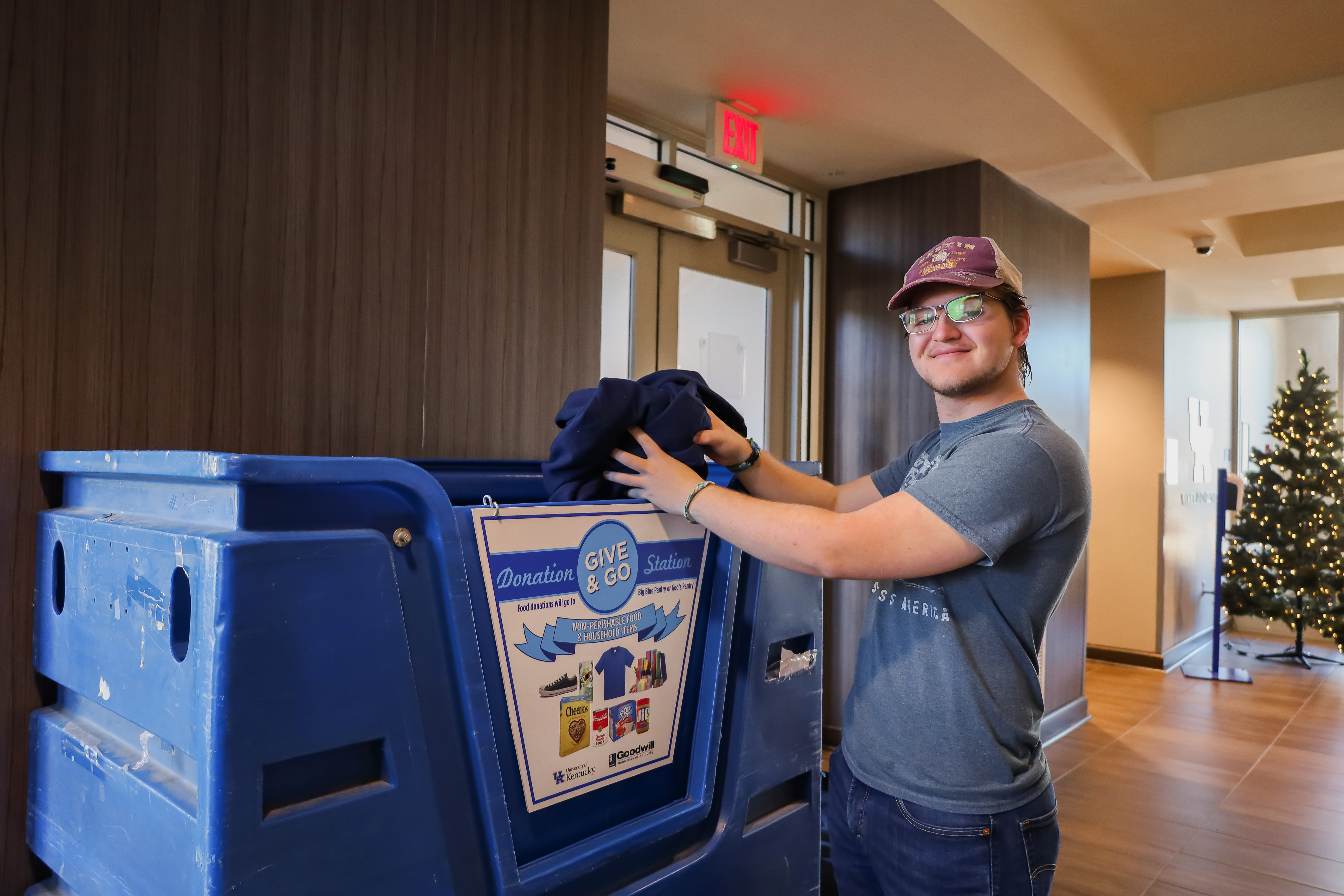 a male student smiling as he puts clothes in a blue bin with a sign that says Give and Go Donation Station