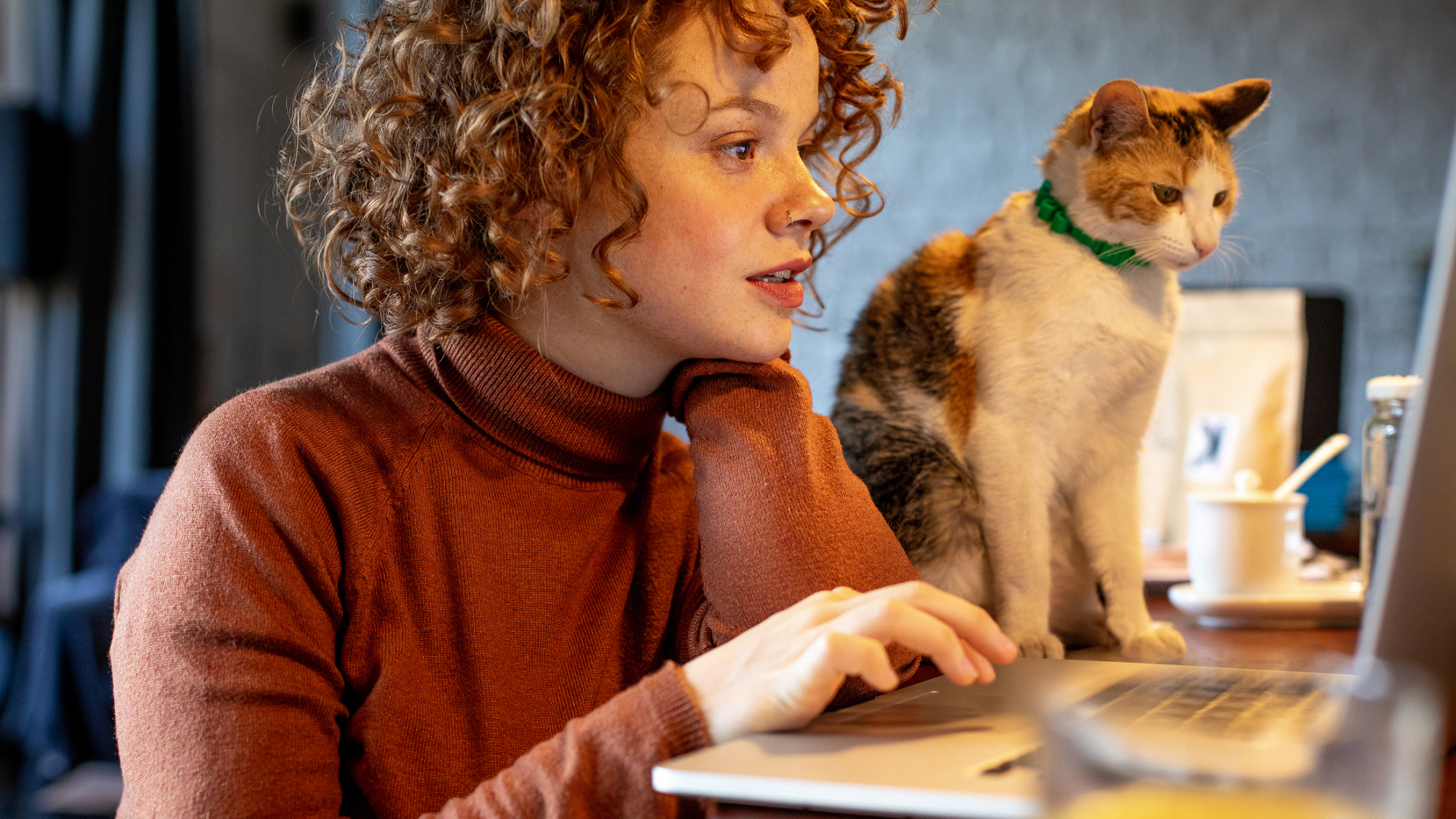 Woman working on computer with cat by her side.