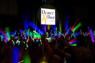 Dance Blue participants in a dark room with glow sticks dancing under a Dance Blue sign.