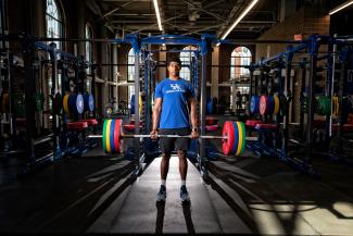 A male student lifting a bar of weights in the Alumni Gym.