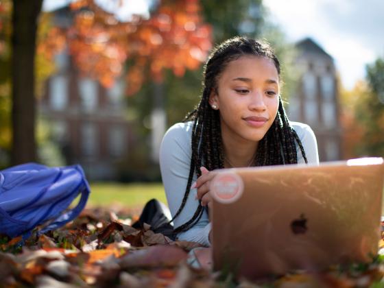 A student works on her macbook outside on campus in the fall.