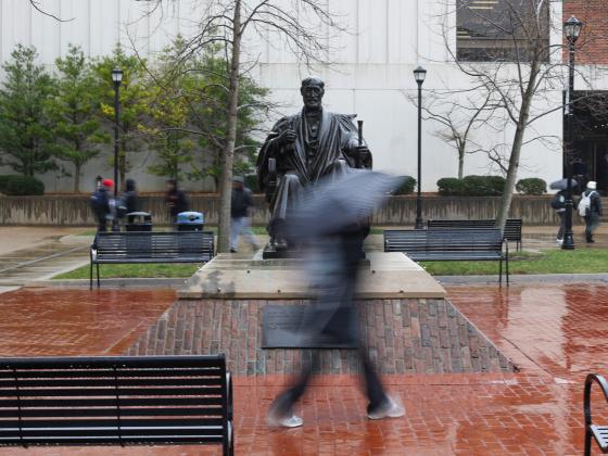 a UK student walking on campus in the rain with a black umbrella