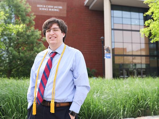 Male student with graduation cords standing in front of building